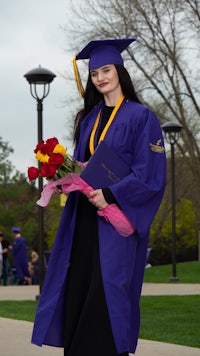 a woman in a graduation gown holding a bouquet of flowers